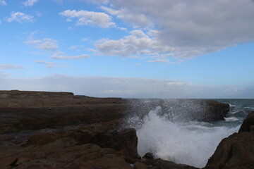 Sea waves impacts on this rock platform down below from the Norah head lighthouse in Central Coast Australia. Blue and white sky formations in the horizon.
