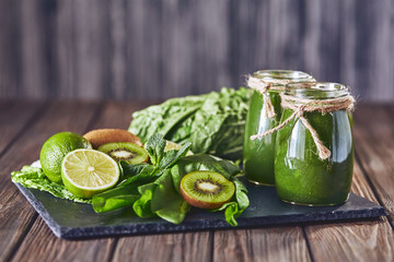 Blended green smoothie with ingredients on the stone board, wooden table selective focus