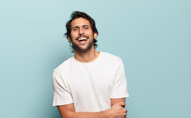 young handsome indian man laughing shyly and cheerfully, with a friendly and positive but insecure attitude