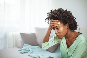 Close up african female sit on couch feels unhappy desperate thinking about personal difficulties...