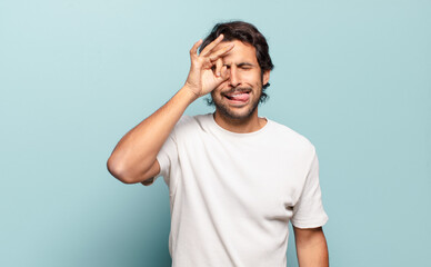 young handsome indian man smiling happily with funny face, joking and looking through peephole,...