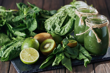 Blended green smoothie with ingredients on the stone board, wooden table selective focus