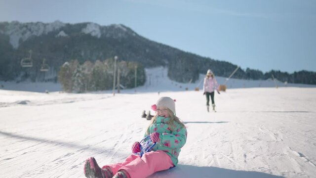 Slow motion - Little girl sledding down the hill and having fun in a snow park
