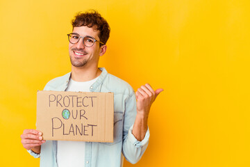 Young caucasian man holding a protect our planet placard isolated points with thumb finger away, laughing and carefree.