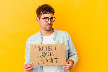 Young caucasian man holding a protect our planet placard isolated confused, feels doubtful and unsure.