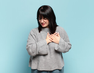 plus size pretty woman looking sad, hurt and heartbroken, holding both hands close to heart, crying...
