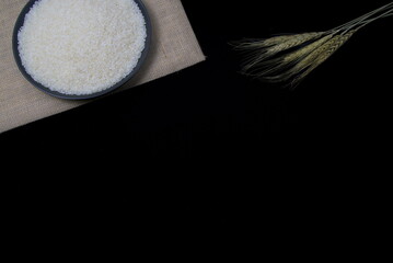 Wheat ears and white rice on the plate on black background, organic food, copy space