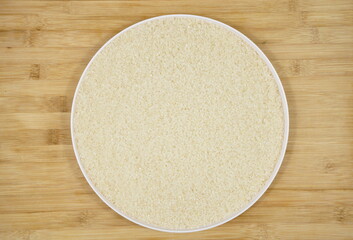 Uncooked white rice on a round plate, top view, wooden background
