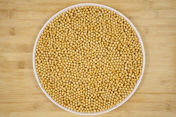 Closeup of organic soybeans on round white porcelain plate on wooden background, top view, healthy legume