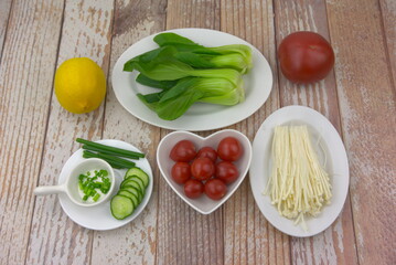 Organic ingredients on the table. Bok choy, chopped green onion, enoki mushroom, cucumber slices, cherry tomatoes, tomato and lemon. Various side dishes