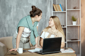 Two happy students chatter and gossip. Young girls are preparing for the exam with the help of laptop. Student life, the concept of education.