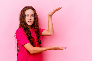 Little caucasian girl isolated on pink background shocked and amazed holding a copy space between hands.