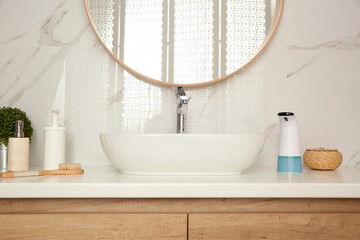 Modern automatic soap dispenser and other toiletries on countertop in bathroom