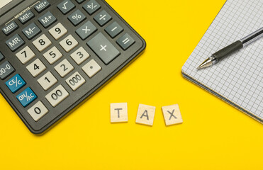 Word tax made with wood letters on yellow background and modern calculator with pen and notebook....