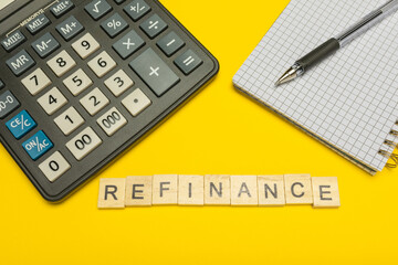 Word refinance made with wood letters on yellow background and modern calculator with pen and...