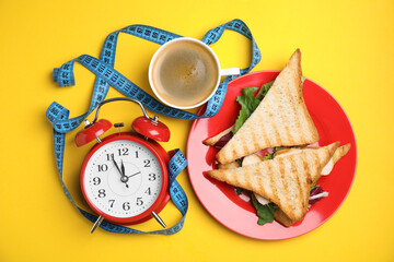 Flat lay composition with tasty sandwiches and alarm clock on yellow background. Nutrition regime