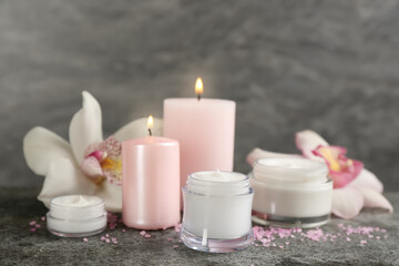 Fototapeta na wymiar Beautiful spa composition with cosmetic products, candles and flowers on grey table