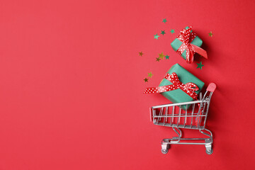 Small shopping cart with gift boxes on red background, flat lay. Space for text © New Africa