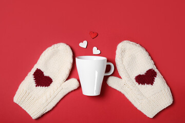 Obraz na płótnie Canvas Knitted mittens, cup and paper hearts on red background, flat lay