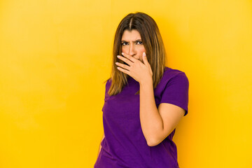 Young indian woman isolated on yellow background covering mouth with hands looking worried.