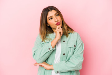 Young indian woman isolated on pink background looking sideways with doubtful and skeptical expression.