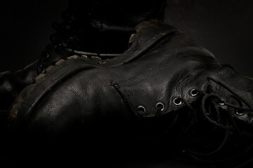 A pair of old, worn, black leather army boots, with traces of dirt and mud on them.