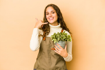 Young caucasian gardener woman holding a plant isolated showing a mobile phone call gesture with fingers.