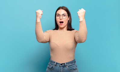 young pretty casual woman celebrating an unbelievable success like a winner, looking excited and...