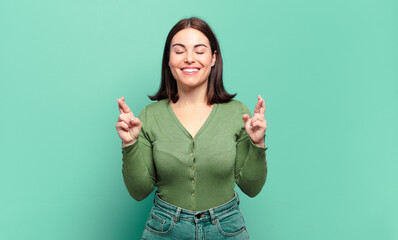 young pretty casual woman smiling and anxiously crossing both fingers, feeling worried and wishing...