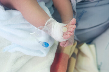 Fototapeta premium newborn baby's leg wrapped in a cotton swab and a needle for medication.