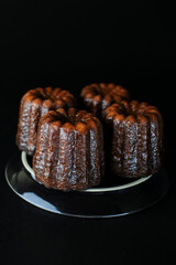 Caneles de bordeaux - traditional French sweet dessert serve with tea or coffee in dark tone on black background.