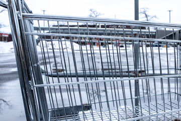 A silver metal shopping cart in a barren parking lot during the middle of winter in London, Ontario, Canada on a gloomy and overcast day.