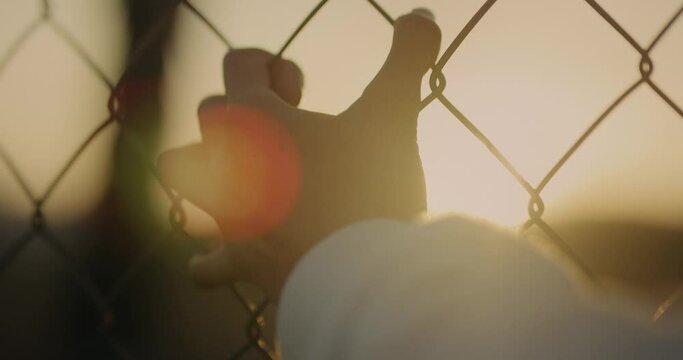 MANO EN ATARDECER AGARRANDO UNA REJA. MIRANDO EL SOL. CLOSE UP DE MANO