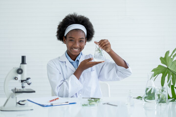 Young African American Scientist present flask with plant inside, smile and look to camera with other tools in laboratory and experiment with plant tissue science concept.