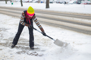 clearing snow from the pavement in front of the house, snow removal,  woman in a colorful cap with a snow shovel