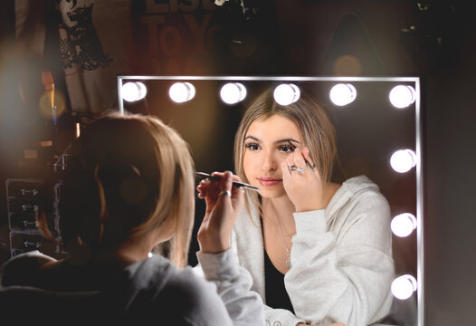 Young teenage girl doing make up shaping her eye brows in front of vanity mirror with lights