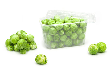 Organic brussels sprouts in disposable plastic container and outside it isolated on white background.