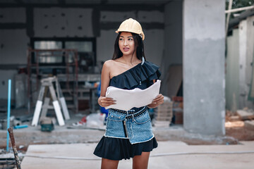 Amazing black haired girl engineer in helmet and dress is designing a new building, portrait