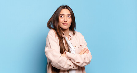 young pretty casual woman shrugging, feeling confused and uncertain, doubting with arms crossed and...