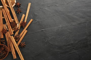 Aromatic cinnamon sticks and anise on black table, flat lay. Space for text