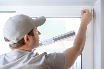 Fototapeta na wymiar Man installing gray pleated blinds on the window