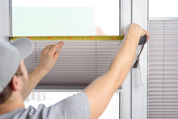 Man installing gray pleated blinds on the window - obrazy, fototapety, plakaty