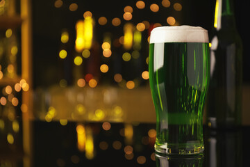 Glass of green beer on black table against blurred lights, space for text. St Patrick's Day...