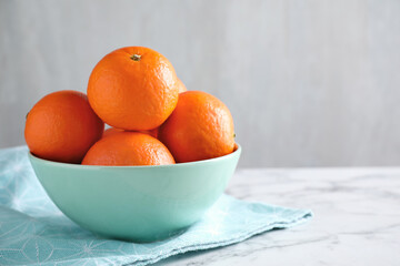 Delicious ripe tangerines in bowl on white marble table. Space for text