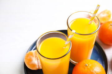 Glasses of fresh tangerine juice and fruits on white table