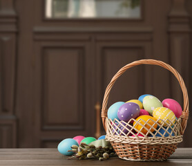 Wicker basket with bright painted Easter eggs on wooden table indoors, space for text