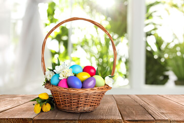 Wicker basket with bright painted Easter eggs and spring flowers on wooden table