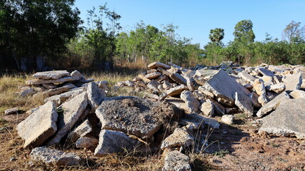 Fototapeta na wymiar A large pile of slabs. Concrete debris from the old road demolition and left on the ground. On a green tree background and blue sky with copy space. Selective focus
