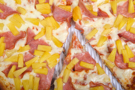 Top View Flat Lay Of One Whole Sliced Hawaiian Pizza In The Box. Covered With Canadian Bacon, Also Known As Ham, And Pineapple. Close Up With One Slice Pulled Separated From The Whole.