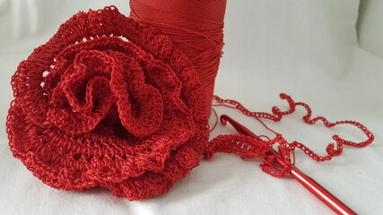 A red cone of crochet thread and a rose, a finished piece of crocheted work and a red crochet...